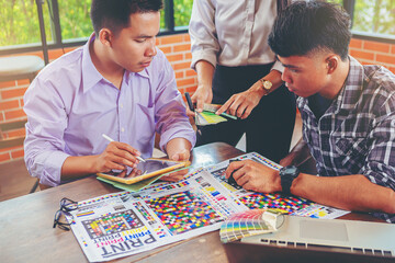 Team graphic designer checking print quality of media graphics proof print and color guides in...