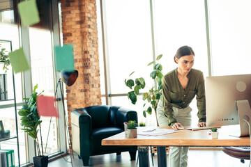 Young businesswoman working in a stylish office space, focusing on her tasks with determination and...
