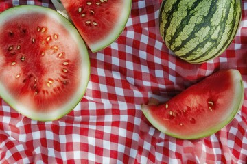 Sliced watermelon on a red gingham picnic blanket outdoors