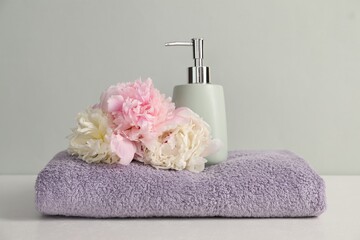 Soft towel, peony flowers and liquid soap on light grey background