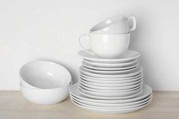 Different clean dishware on light wooden table near white wall