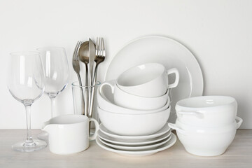 Different clean dishware on light wooden table near white wall