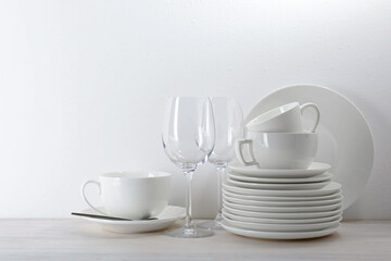 Different clean dishware on light wooden table near white wall
