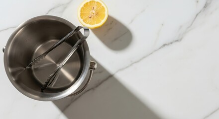 Stainless steel mixing bowl with a lemon on a marble countertop. The bowl has a whisk attached, creating a clean and modern kitchen scene.