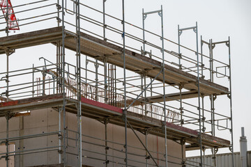 Scaffold around a concrete building. Reinforcement bars can be seen inside. Red crane boom behind.