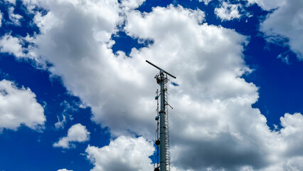 Telecom tower pierces cerulean tapestry under fluffy cumulus parade, echoing World...