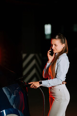 Woman charges electric car while talking on the phone under vibrant neon lights