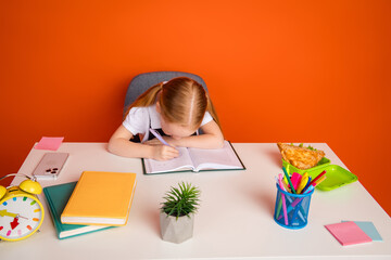 Young schoolgirl diligently studying at a desk with art supplies, books, and an orange background...