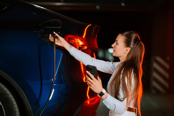 Woman charges electric car in vibrant neon lighting during nighttime
