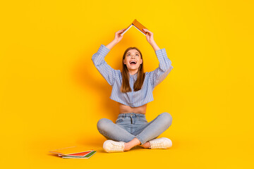 Young woman holding book above head and smiling with joy against a vibrant yellow background