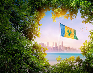 Saint Vincent and the Grenadines flag waving with modern skyline. A flag blow behind the tree leafs. Saint Vincent and the Grenadines national flag for independence day.