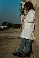 Young female doctor using phone while leaning on hospital wall
