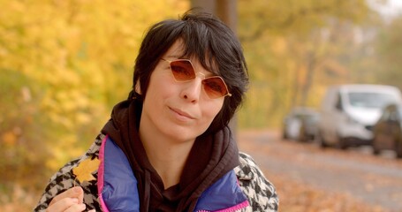 In autumns crisp air, a woman stands among vibrant yellow leaves, holding a colorful leaf as a...