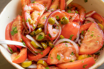 Fresh and simple summer tomato salad in a bowl. Close-up image of juicy red tomatoes with herbs,...