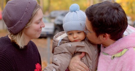 A lovely family scene in a vibrant autumn park shows a child held by one parent while the other...