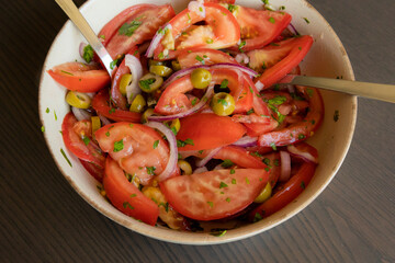 Fresh and simple summer tomato salad in a bowl. Close-up image of juicy red tomatoes with herbs,...