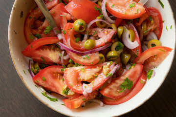 Fresh and simple summer tomato salad in a bowl. Close-up image of juicy red tomatoes with herbs,...