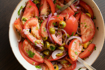 Fresh and simple summer tomato salad in a bowl. Close-up image of juicy red tomatoes with herbs,...