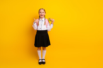 Cheerful schoolgirl with braids smiling while holding a sandwich and giving a thumbs up against a...