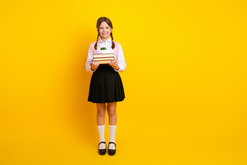 Smiling schoolgirl in uniform holding book against a bright yellow background symbolizes education...