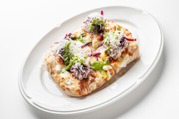 Flatbread pizza with melted cheese, meatballs, cabbage, and green sauce on a white plate, top view. Tasty, colorful dish with a rustic and homemade presentation.