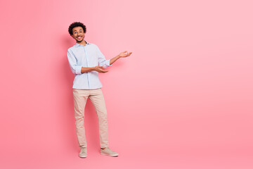 Smiling young man in casual attire gesturing on a pink background, showcasing elegant style and...
