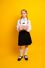 Young schoolgirl holding book in front of yellow vertical background dressed in formal uniform...