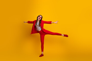 Attractive young woman in a red suit joyfully posing against a bright yellow background, showcasing stylish fashion and positive energy