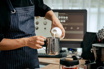 A young Asian male barista, dressed in a striped apron, skillfully creates beautiful latte art in a cozy, modern cafe, professional coffee equipment and takeaway cups.