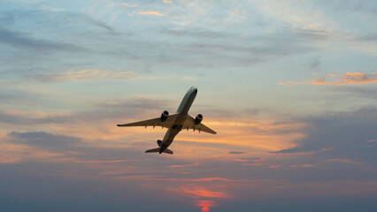 Airplane flying above dramatic sunset sky background.