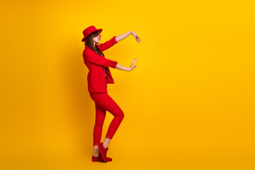 Attractive young woman wearing a red suit posed against a vibrant yellow background expressing...