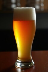 Amber Ale in Tulip Glass: A refreshing amber ale, exhibiting a rich, golden hue and a thick, creamy head, rests in a classic tulip glass on a dark wooden surface.