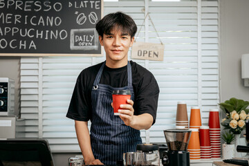 A young Asian male barista, dressed in a striped apron, skillfully creates beautiful latte art in a...
