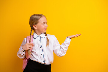 Cheerful young schoolgirl gesturing on a vibrant yellow backdrop promoting education and...