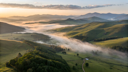 Aerial view of forested mountain peaks emerging from a thick sea of clouds at sunrise. The soft mist flows between the hills, creating a surreal, dreamlike atmosphere with warm light on the horizon. P