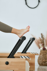 Unrecognizable female athlete exercising on a pilates machine with her bare feet pressing onto a...
