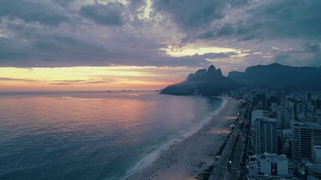 Breathtaking aerial views of Ipanema Beach at sunset in Rio de Janeiro, capturing the vibrant sky, ocean waves, city lights, and iconic Dois Irm&atilde;os mountains.