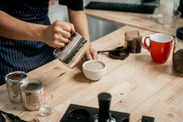 A young Asian male barista, dressed in a striped apron, skillfully creates beautiful latte art in a cozy, modern cafe, professional coffee equipment and takeaway cups.