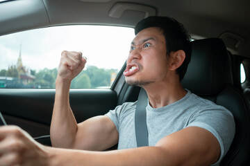 Asian man yelling and shaking fist while driving, angry driver
