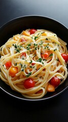 Vibrant linguine pasta with colorful cherry tomatoes, garnished with fresh herbs, elegantly served in a dark ceramic bowl against a sleek background