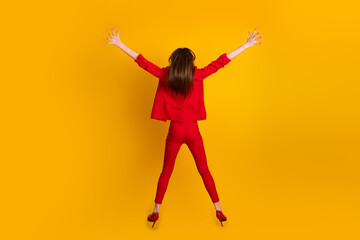 Young woman in trendy red suit posing energetically against vibrant yellow backdrop, showcasing modern style and confidence