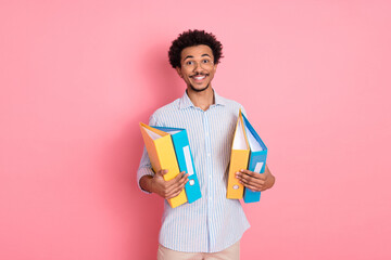 Smiling young man holding colorful folders against a vivid pink background, showcasing stylish...