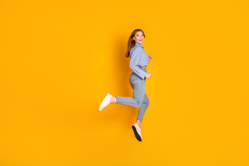 Cheerful young woman in casual fashion jumping with happiness against vibrant yellow background...