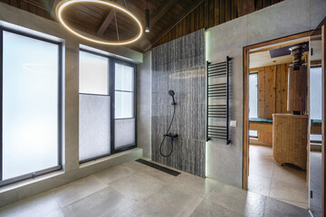 This bathroom showcases a sleek shower with modern fixtures, large windows allowing natural light, and a blend of stone and wood elements for a warm atmosphere.