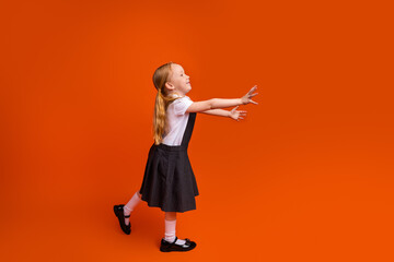 Cheerful young schoolgirl with red hair and uniform joyfully stretching hands in playful pose...