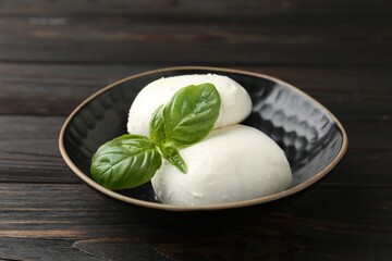 Pieces of delicious mozzarella cheese and basil in bowl on wooden table, closeup