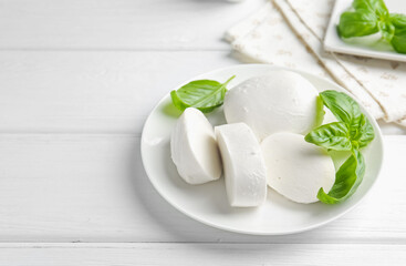 Pieces of delicious mozzarella cheese and basil on white wooden table. Space for text