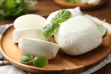 Pieces of delicious mozzarella cheese and basil leaves on wooden table, closeup