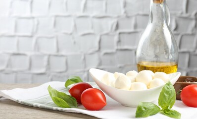 Tasty mozzarella cheese balls, tomatoes, basil, oil and peppercorns on wooden table, closeup