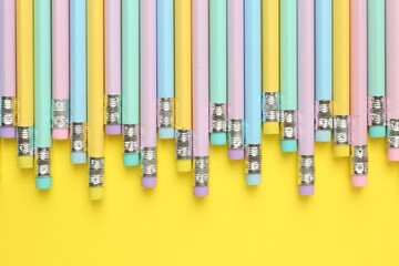 Many graphite pencils with erasers on yellow background, flat lay. Space for text